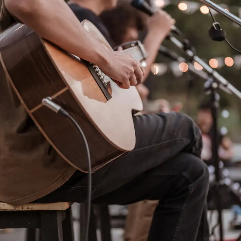 Gitarrist spielt auf einer Bühne mit Mikrofonen bei einer Outdoor-Veranstaltung mit stimmungsvoller Beleuchtung.